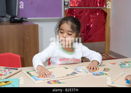 4 ans fille de l'école pré assis à une table faisant un puzzle Banque D'Images