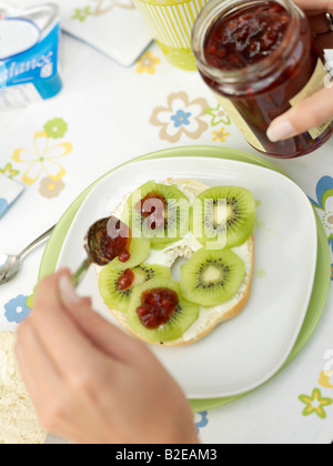 Close-up of person's hand putting confiture sur tranches de kiwi Banque D'Images