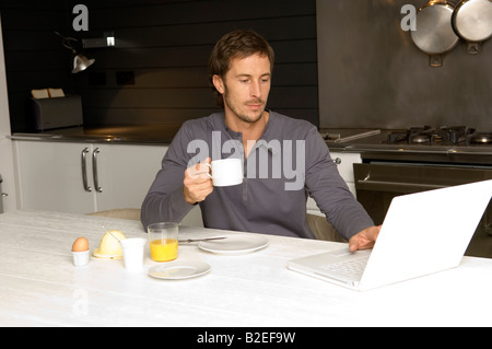 Mid adult man travaille sur un ordinateur portable et prendre le petit-déjeuner dans la cuisine Banque D'Images
