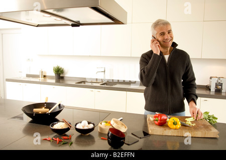 Portrait of a young man talking on a mobile phone dans la cuisine Banque D'Images