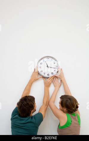 Vue arrière d'un couple en train de monter une horloge sur le mur Banque D'Images