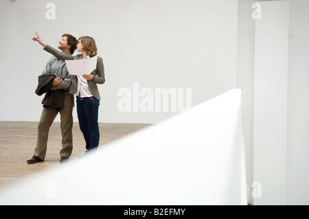 Jeune femme debout dans une salle et en pointant avec un mid adult man standing à côté d'elle Banque D'Images