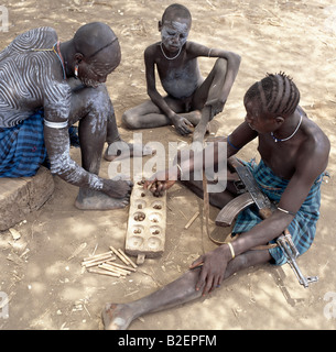 Deux hommes Mursi avec des modèles de jouer un jeu de bau comme un jeune garçon les regarde. Banque D'Images