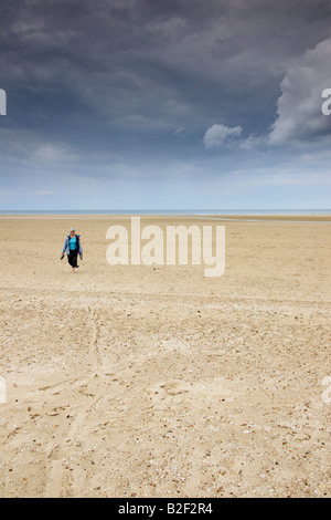 Une femme marche sur la vaste étendue d'une plage de North Norfolk, Angleterre. Banque D'Images