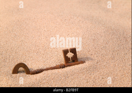 Une vieille clé rouillée partie enterrée dans le sable Banque D'Images