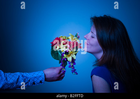 Femme sentant les fleurs offertes pour elle à un bras tendu de l'homme Parution Modèle Banque D'Images