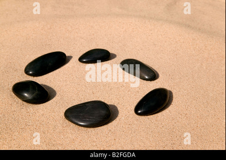 Six cailloux lisses noires disposées en cercle sur une plage de sable fin Banque D'Images