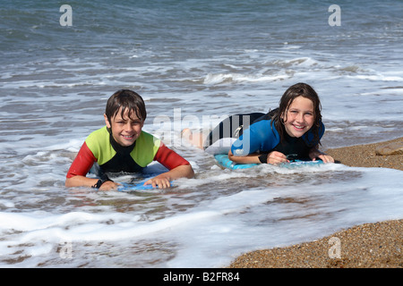 Deux adolescents à l'aide body boards dans le surf à Burton Bradstock Dorset portant des combinaisons Banque D'Images