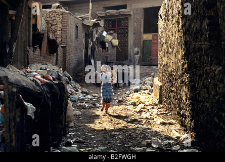 Peu zabbaleen fille marchant dans une allée bordée d'ordures, ville des morts slum Banque D'Images