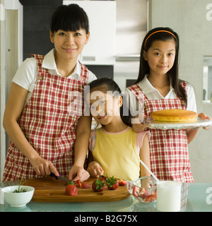 Portrait of a Mid adult woman avec ses deux filles de préparer des aliments dans une cuisine Banque D'Images