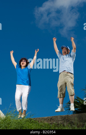 Low angle view of a senior man with a young woman jumping avec leurs bras levés Banque D'Images