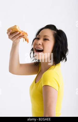 Portrait d'une jeune femme mangeant une tranche de pizza et souriant Banque D'Images