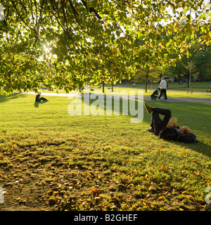 Un homme la lecture d'un livre réside dans l'herbe le soir de l'automne ensoleillé de St.James Park London England UK Banque D'Images