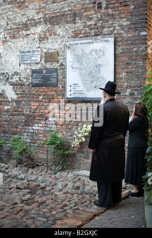 Un homme juif hassidique et son épouse tiennent en face de l'un des deux autres pièces du mur du Ghetto de Varsovie. Banque D'Images