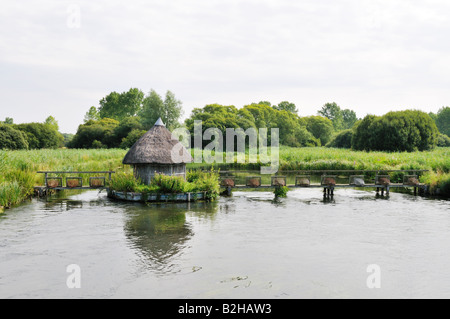 Test de la rivière près de Longstock Hampshire Angleterre fishermans hut de chaume et osier pièges à anguilles de l'autre côté de la rivière Banque D'Images