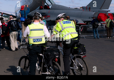 2 Deux hommes de police sur bicyclettes dans la région de yellow jackets assis à parler lors d'une manifestation publique au Farnborough Air Show close up Banque D'Images