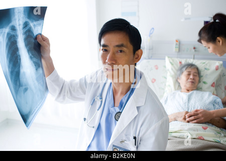 Portrait d'un homme médecin examinant un rapport des rayons X avec deux femmes à l'arrière-plan Banque D'Images