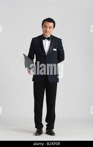 Portrait of a waiter holding un menu et standing with hands behind back Banque D'Images
