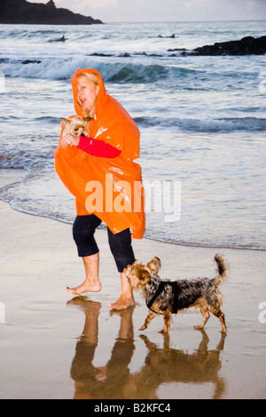 Young woman wearing une orange kagool marcher ses deux chiens Yorkshire Terrier le long de la côte à Harlyn Bay, Cornwall, Angleterre Banque D'Images