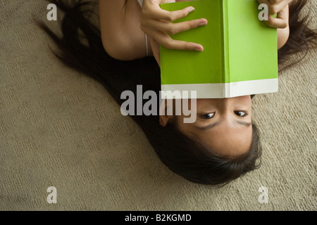 Portrait d'une jeune femme étendue sur le sol et tenant un livre Banque D'Images