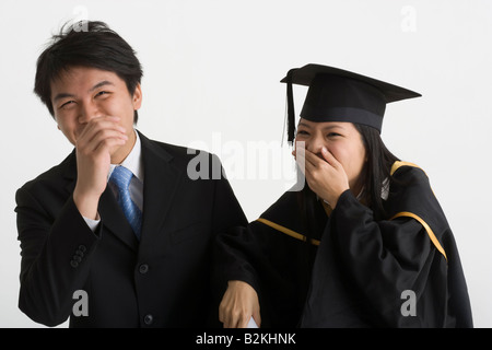 Jeune homme et une jeune femme diplômé rire avec couvrant leur bouche Banque D'Images