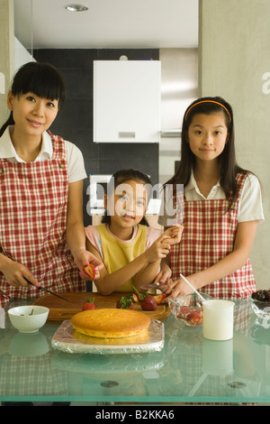 Portrait of a Mid adult woman avec ses deux filles de préparer des aliments dans une cuisine Banque D'Images