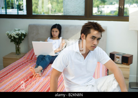 Portrait d'un jeune homme à la grave avec un mid adult woman using a laptop dans l'arrière-plan Banque D'Images