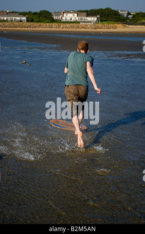 Un jeune homme sur la plage d'embarquement écrémé Kid Skimboarder Coucher de soleil Océan Surf Plage Plages nord-américain US USA Cape Cod Banque D'Images