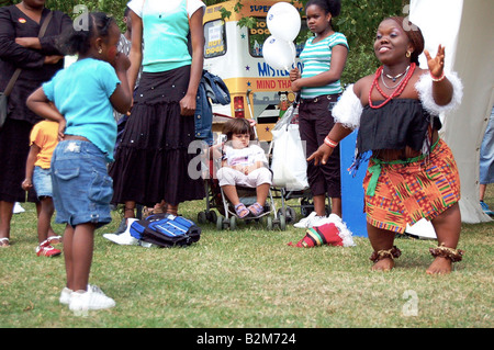 Une jeune fille timide se transforme au cours d'une séance de danse africaine avec un nain tribal dancer à Londres contre le racisme festival. Banque D'Images