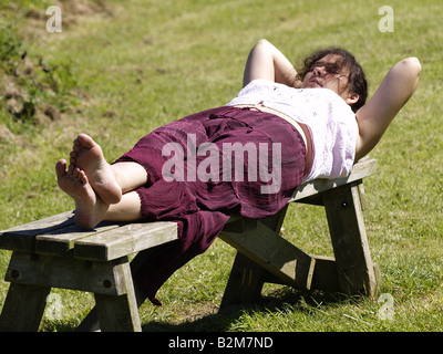 Femme endormie sur un banc de parc sous le soleil d'après-midi Banque D'Images