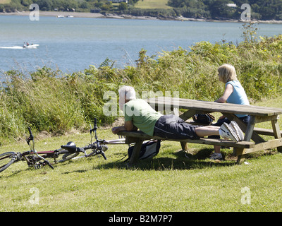 Couple 50s sur un banc de parc le long de la côte sud-ouest, face à la mer. Padstow, Cornwall, UK Banque D'Images