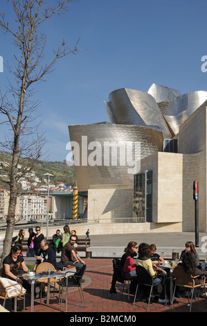 Les jeunes gens assis à des tables de café en plein air en face du musée Museo Guggenheim Bilbao Espagne Art Gallery Banque D'Images