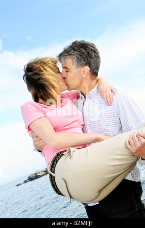 Mature couple de baby-boomers s'embrasser sur une plage Banque D'Images