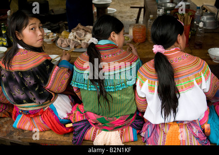 Trois filles de tribu de Hmong de fleurs assis à un stand de nourriture avec le dos à la caméra on regarde sur son épaule dans le marché de Sapa Vietnam Banque D'Images