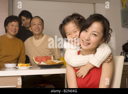 Portrait of a Girl hugging sa mère par derrière avec les membres de sa famille à la table du petit déjeuner Banque D'Images