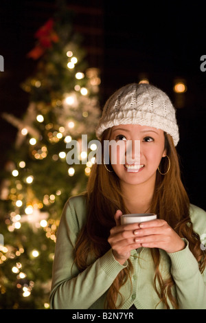 Close-up of a young woman holding une tasse de chocolat chaud devant un arbre de Noël Banque D'Images