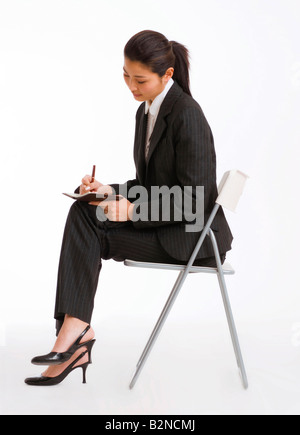 Portrait d'une femme assise sur une chaise et de l'écriture dans un journal Banque D'Images