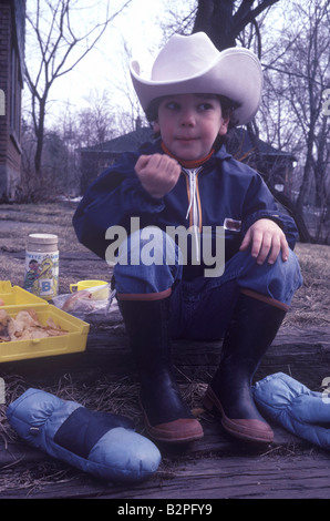 Retro photo de boy wearing cowboy hat et bottes en train de déjeuner. Banque D'Images