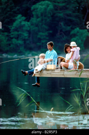Papa et maman avec deux enfants et famille chien assis sur la jetée au bord du lac durant la pêche en Suède de pique-nique Banque D'Images