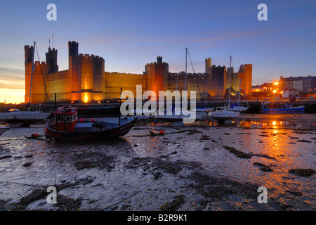 Château de Caernarfon, sur la côte du nord du Pays de Galles éclairés la nuit avec les bateaux dans l'estuaire a échoué sur la marée basse Banque D'Images