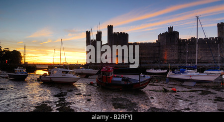 Château de Caernarfon, sur la côte du nord du Pays de Galles éclairés la nuit avec les bateaux dans l'estuaire a échoué sur la marée basse Banque D'Images