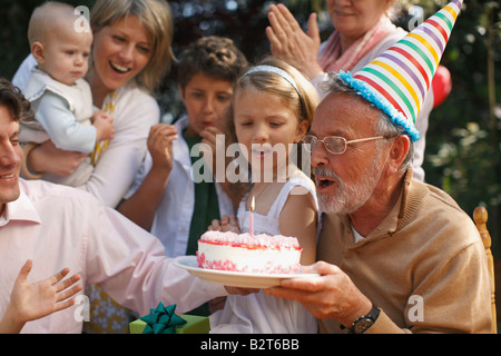 Grand-père blowing out candles at party Banque D'Images