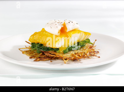 Poisson blanc avec des œufs pochés sur lit de feuilles vertes et de pommes de terre lambeaux Banque D'Images