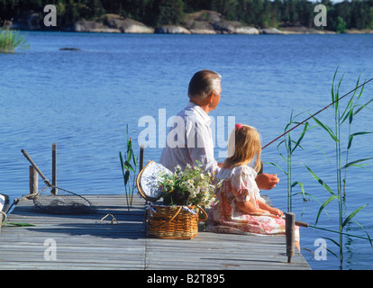 Panier plein de fleurs sauvages et de grand-père avec petit-enfant pêche sur la jetée du lac au cours de l'été suédois Banque D'Images