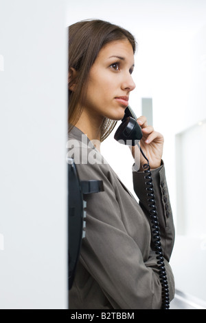 Teen girl leaning against wall, à l'aide de téléphone fixe, à l'écart, side view Banque D'Images