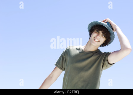 Teenage boy smiling at camera, en mettant sur une hat Banque D'Images