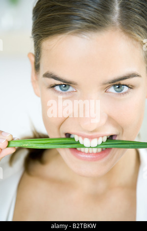 Femme tenant de ciboulette entre les dents, smiling at the camera, portrait Banque D'Images