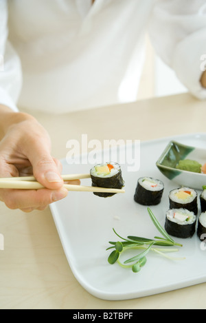 Personne à l'aide de baguettes pour prendre un rouleau de sushi, cropped view Banque D'Images