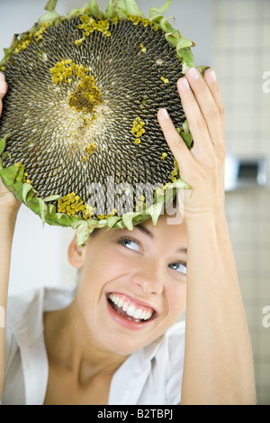 Woman holding up grande tête de fleurs séchées, looking up, smiling Banque D'Images