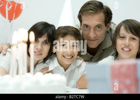 Famille devant le gâteau d'anniversaire avec bougies allumées, smiling at camera Banque D'Images